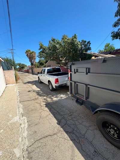 Diamond-plate side of the 777 dump trailer, hitched behind the white Ram 1500 in an alley