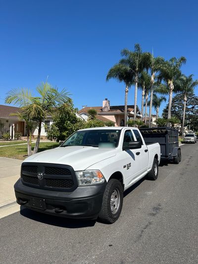 White Ram 1500 pickup hitched to the 777 Junk Removal dump trailer, parked on a palm-lined street