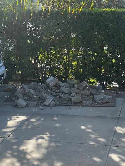 Broken concrete piled on a driveway beside a hedge in Downey before removal